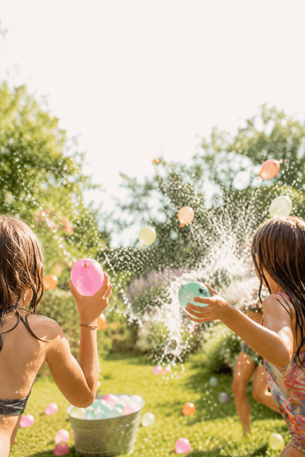 Wasserschlacht: Kinder bei einer Wasserschlacht mit Wasserbällen im Garten