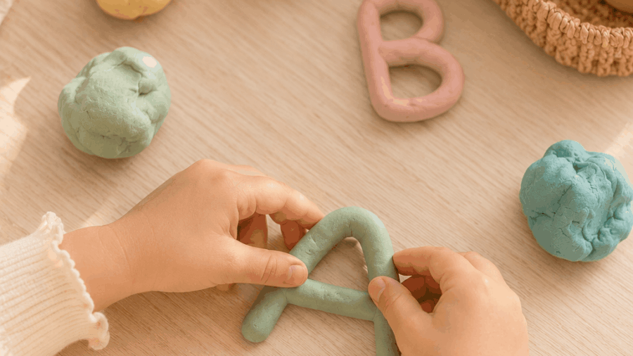 Kinderhände formen Buchstaben aus bunter Knete – Buchstaben lernen spielerisch vor der Schule
