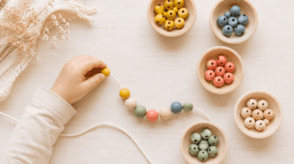 Kinderhand fädelt bunte Holzperlen auf eine Schnur – Feinmotorik und Konzentration spielerisch stärken