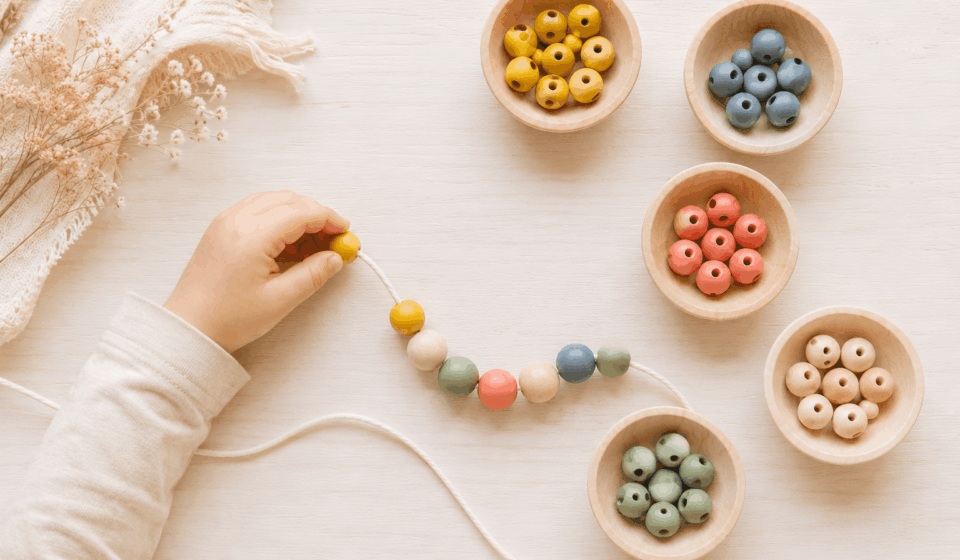 Kinderhand fädelt bunte Holzperlen auf eine Schnur – Feinmotorik und Konzentration spielerisch stärken