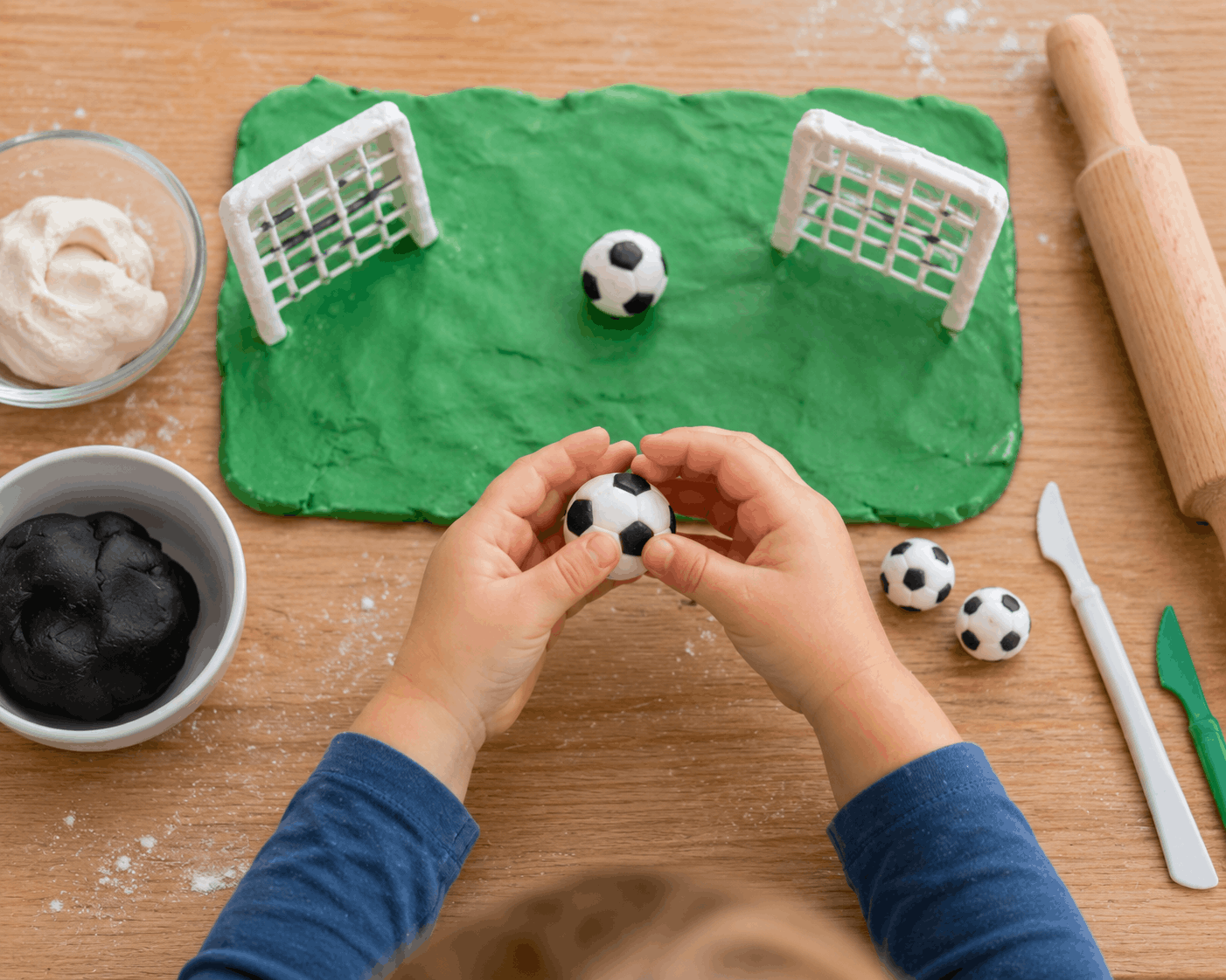 Kinderhände formen kleine Fußbälle und Tore aus selbstgemachter Knete auf einem Tisch. Kreative Fußball-Bastelidee für Kindergartenkinder.